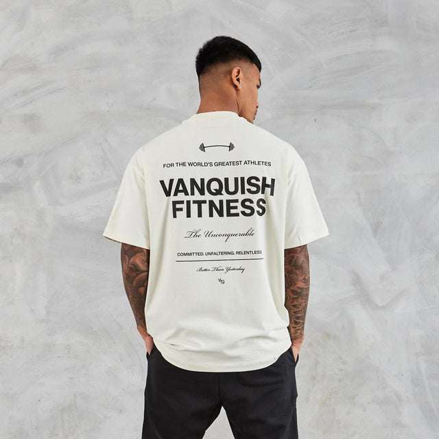 Man wearing white Fitness Boxy Oversized T-Shirt with black text on back, paired with black pants, against gray background